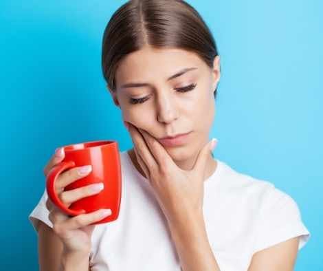 Holding a hot drink with a painful expression